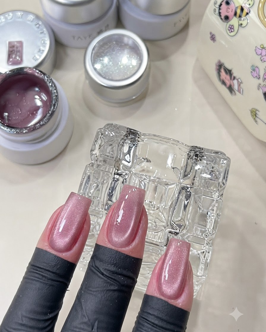 Une main montrant des ongles cat-eye roses catalysés avec un fini scintillant.