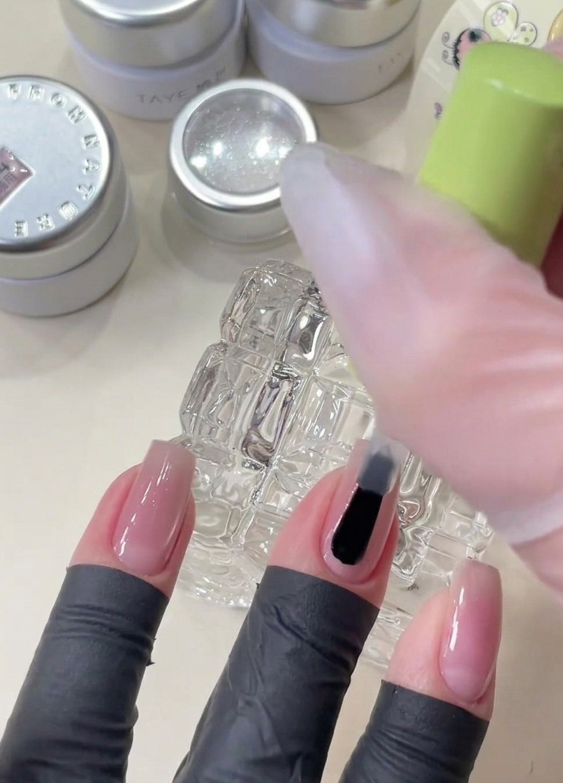 Un pinceau appliquant du gel de base transparent sur un ongle avant de placer des paillettes étoiles décoratives.