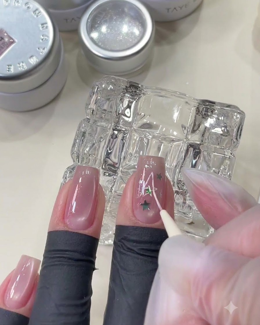 Un pinceau fin dessinant un motif détoile rose sur un ongle orné de paillettes étoiles.