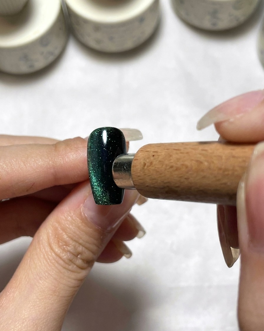 Un outil magnétique positionné près dun ongle cat eye vert foncé pour répartir les pigments.