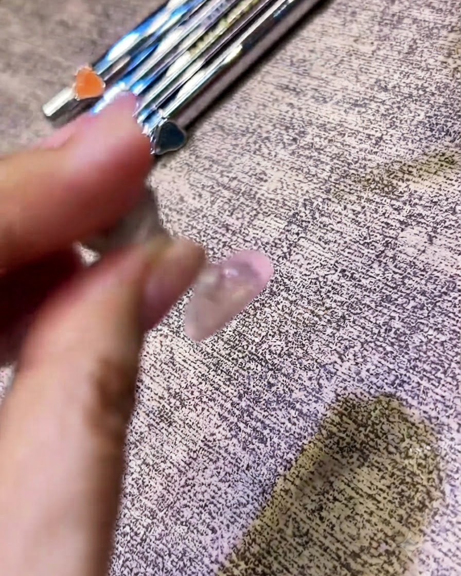 Un pinceau appliquant un top coat transparent sur un ongle à finition chromée.