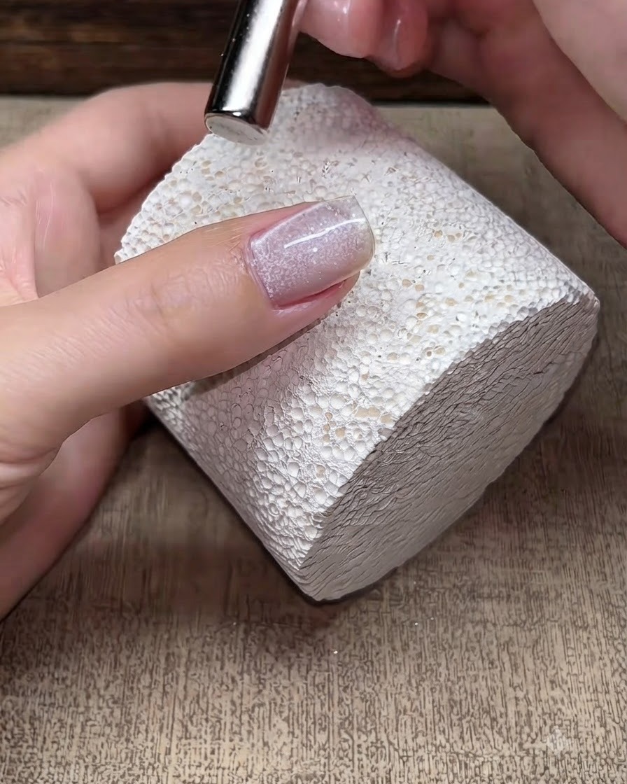 Un petit aimant survolant un ongle en gel cat eye encore humide pour manipuler les particules scintillantes magnétiques.