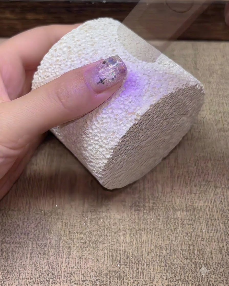 Une main en train de catalyser sous une lampe à ongle UV LED violette.