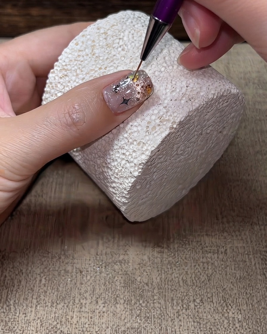 Un pinceau liner fin appliquant un top coat dur autour des bords et dans les interstices des strass sur un ongle fini.