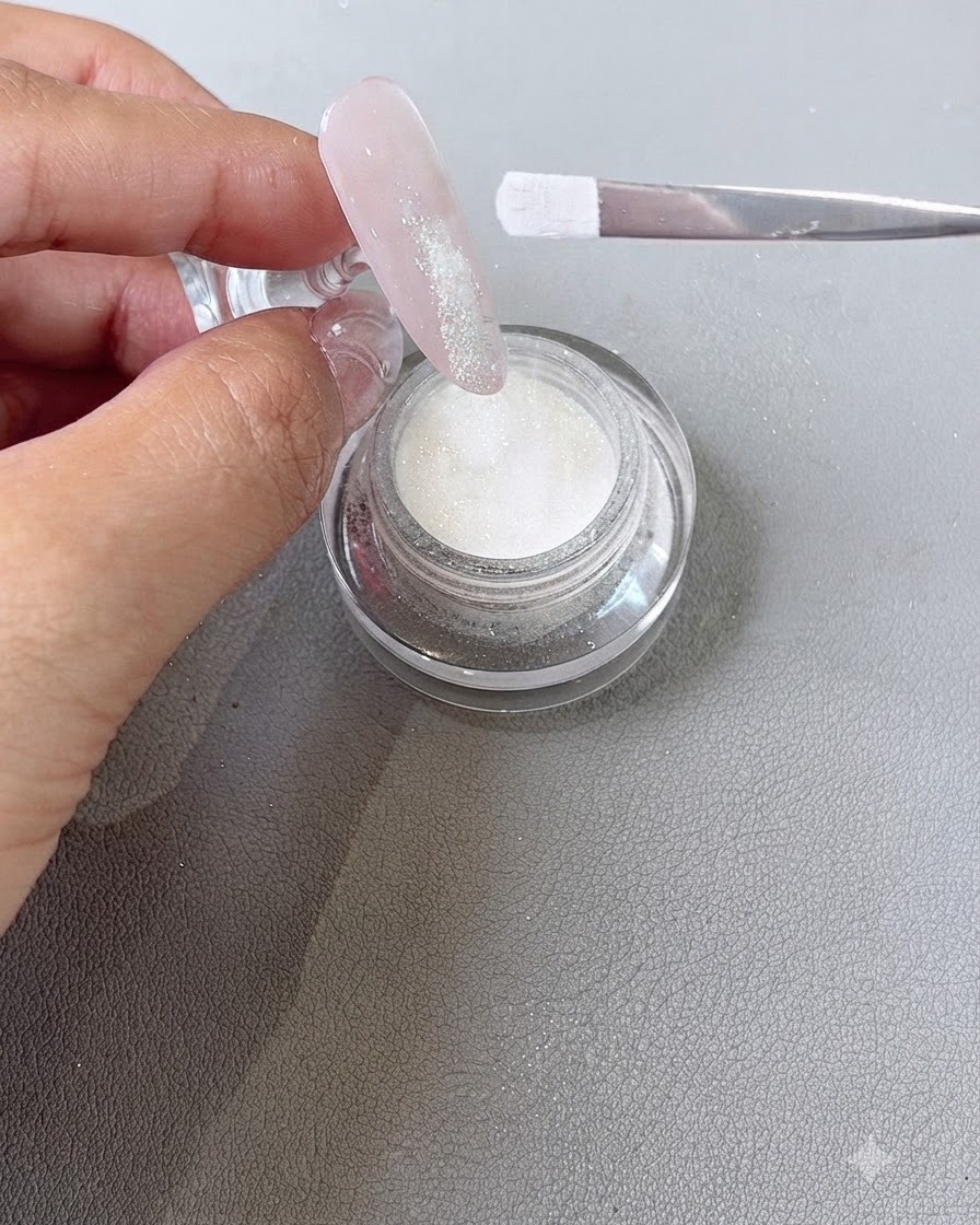 De la poudre de résine saupoudrée à laide dun pinceau sur la zone de pointe en gel humide dun ongle.