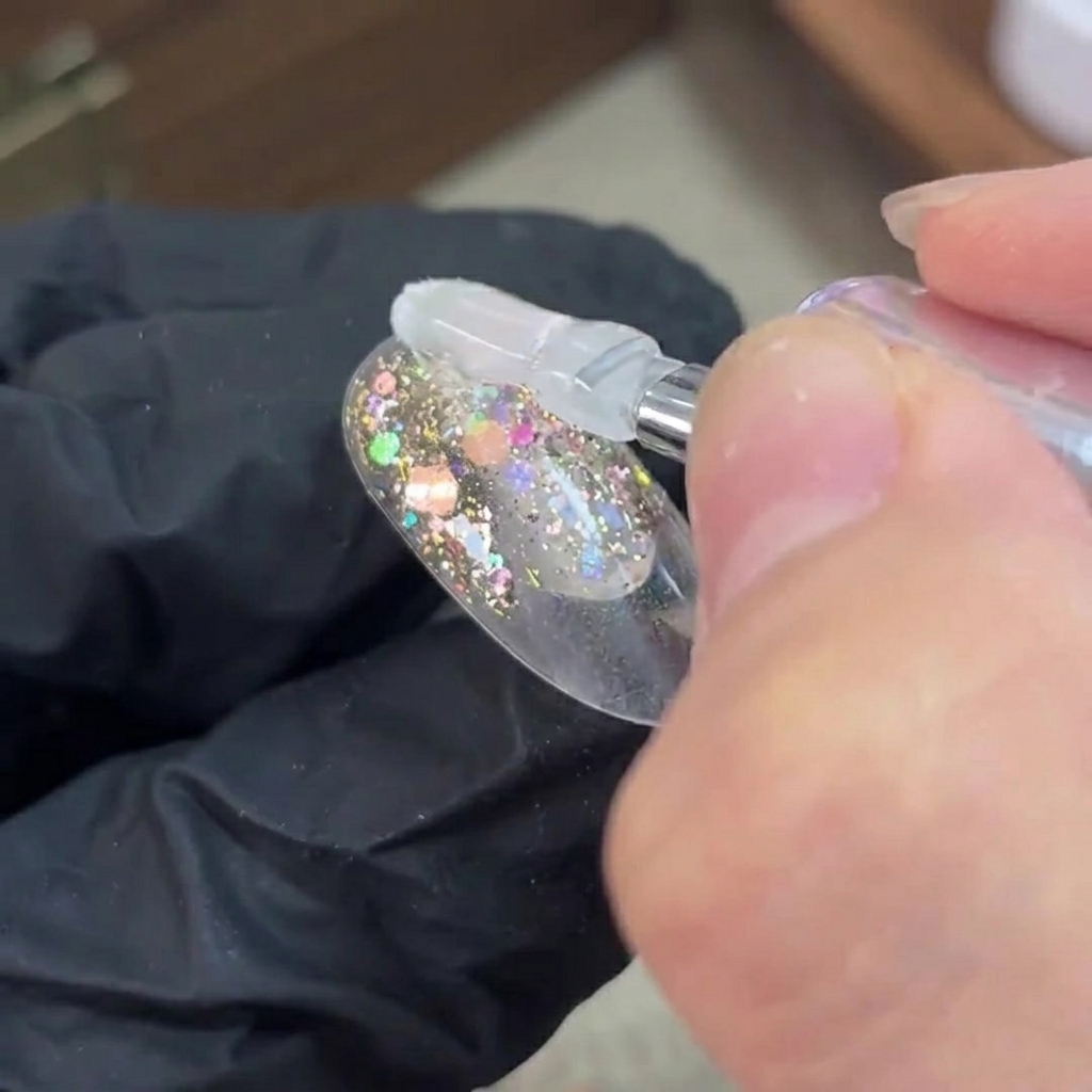 Un pinceau appliquant du gel de base transparent sur une couche de paillettes catalysée sur un ongle.