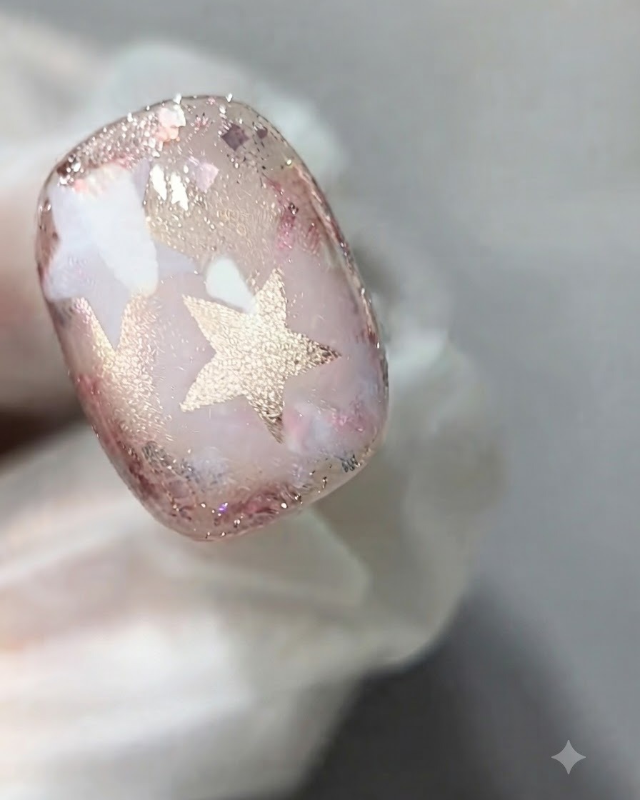 Un pinceau à ongles appliquant une couche de gel œil-de-chat rose diaphane sur la surface dun ongle décoré.