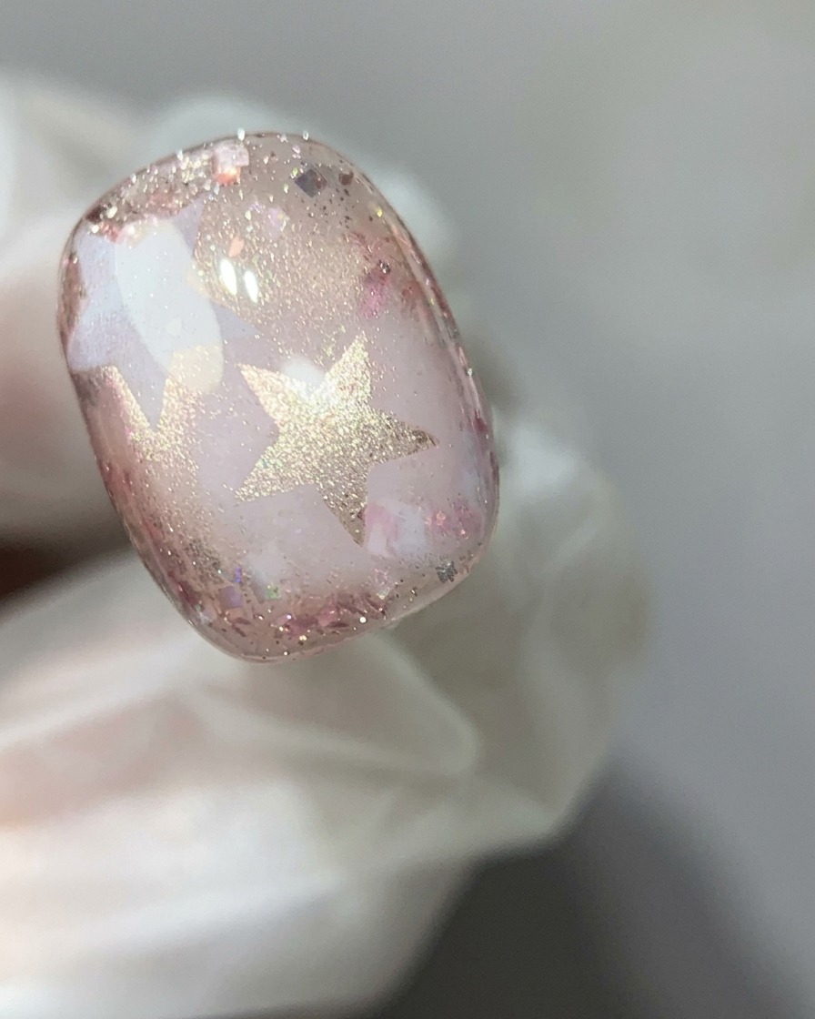 Un bâtonnet aimanté tenu au-dessus dun ongle en gel œil-de-chat rose pour concentrer le reflet chatoyant en un effet de perle de verre.