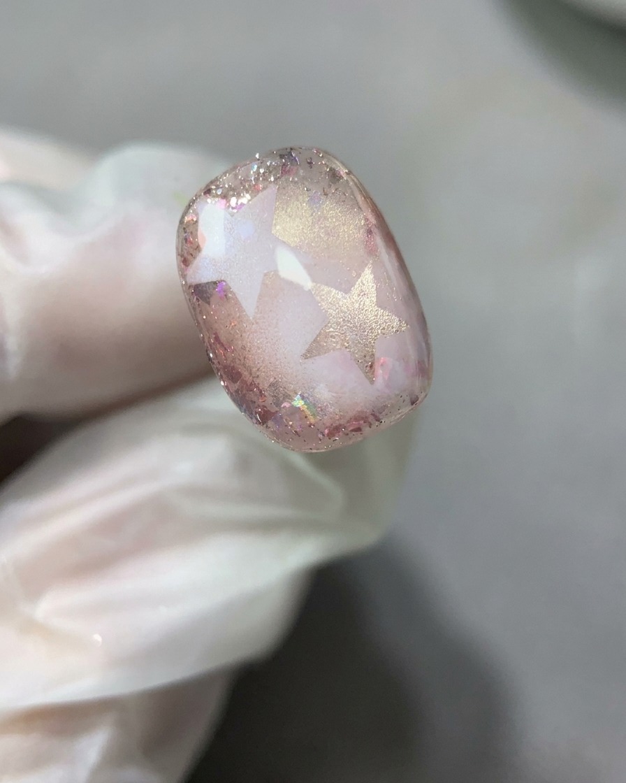 Un pinceau à ongles étalant une fine couche lisse de gel de base transparent sur le motif dongle étoile et paillettes achevé.