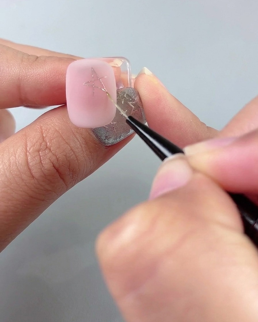 Un pinceau liner fin traçant des lignes pour compléter une forme détoile sur un ongle manucuré rose.