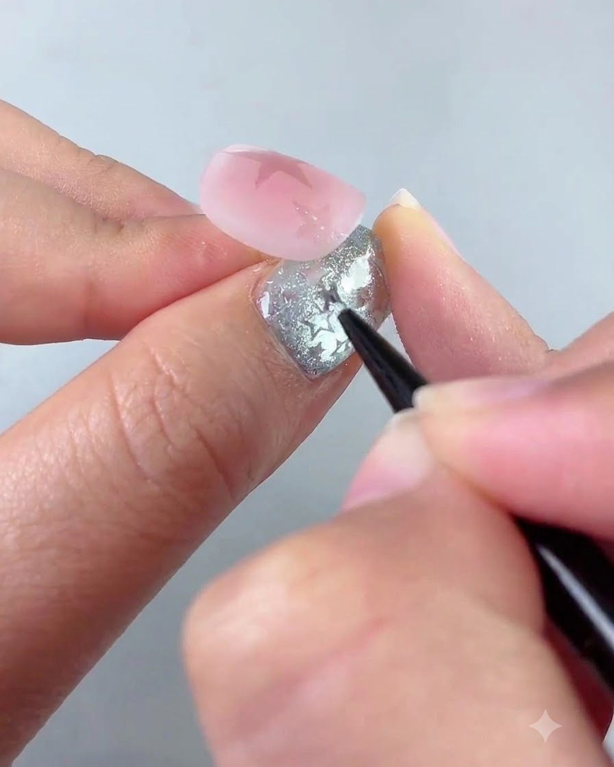 Un pinceau liner détaillant une étoile plus petite près du coin inférieur gauche dun ongle rose.