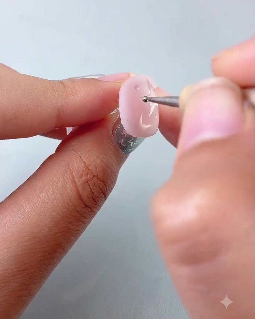 Un stylo à pointer plaquant de petits points daccent autour détoiles peintes sur un ongle rose.