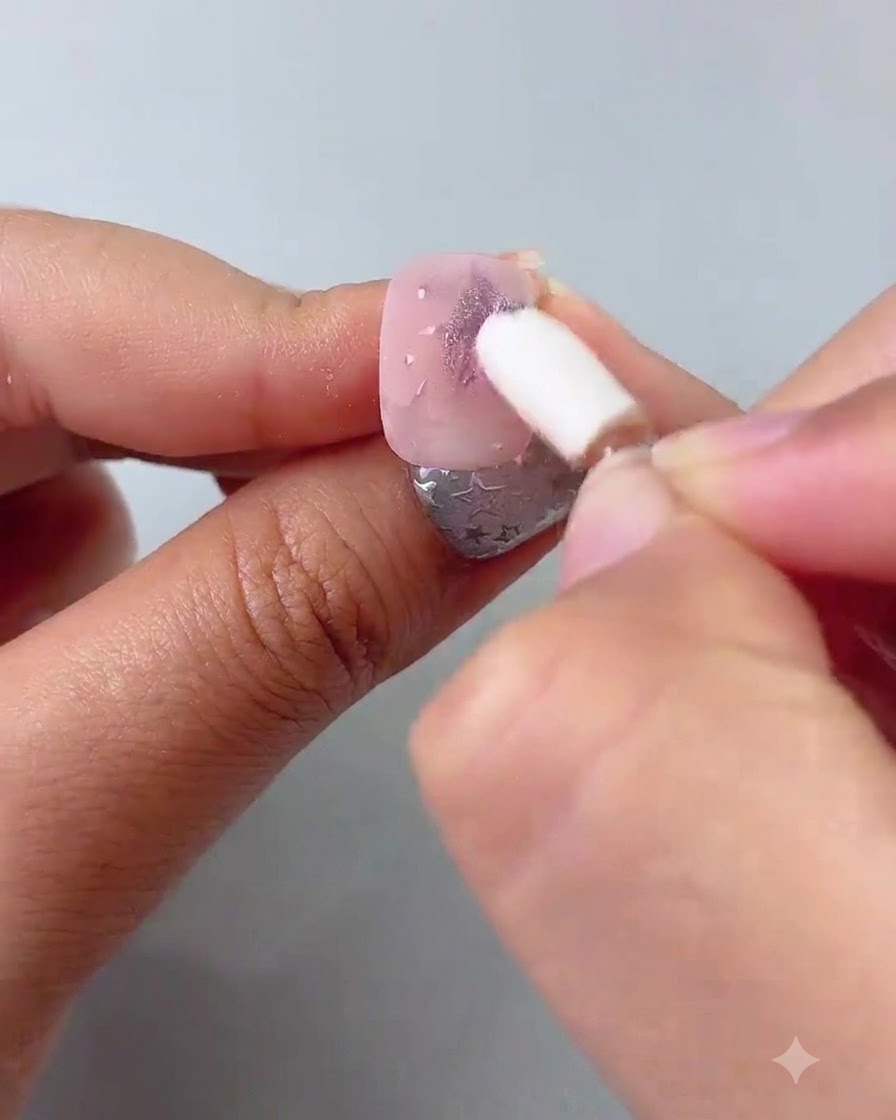 Un applicateur éponge en silicone frottant de la poudre chrome violette sur des étoiles peintes sur un ongle.