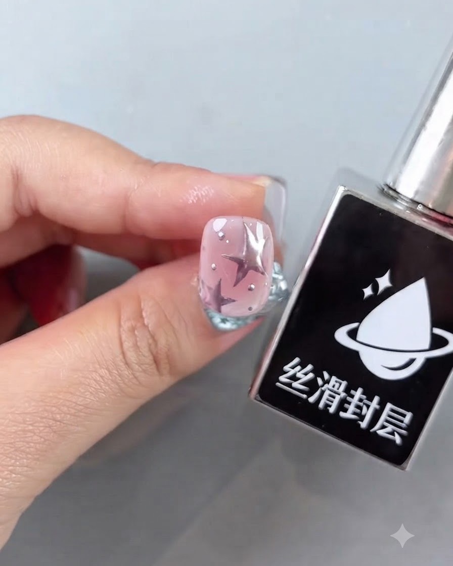 Un flacon de top coat lisse à côté dun ongle rose fini présentant des motifs détoiles et des accents argentés brillants.
