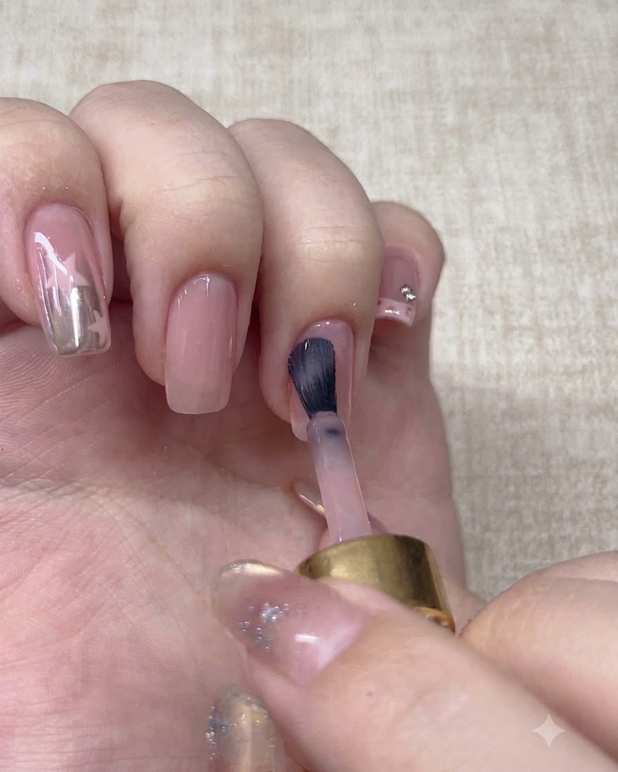 Un pinceau appliquant une seconde couche de vernis de base nude sur longle.