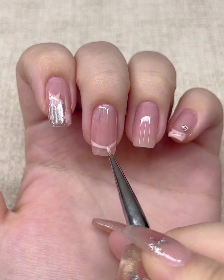 Un pinceau liner fin dessinant une ligne de French manucure rose clair sur un ongle.