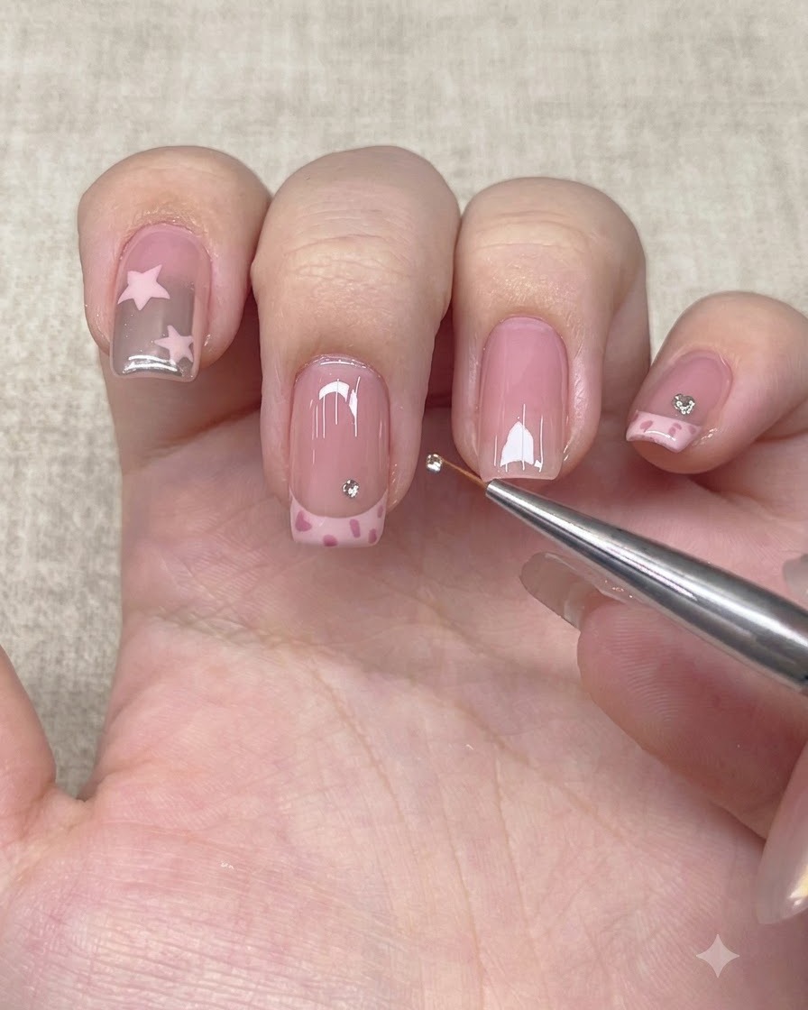 Un outil de précision posant un petit strass juste au-dessus de la ligne de French sur un ongle.