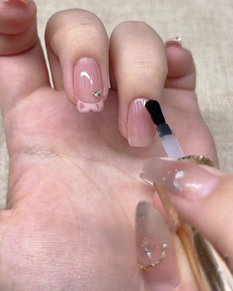 Un pinceau appliquant un top coat transparent sur longle de lannulaire.