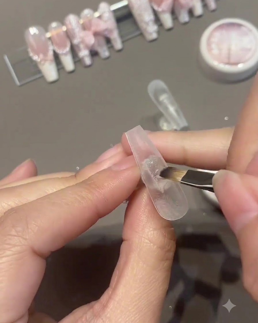 Un pinceau appliquant une seconde couche de vernis gel rose sur la surface dun ongle artificiel.