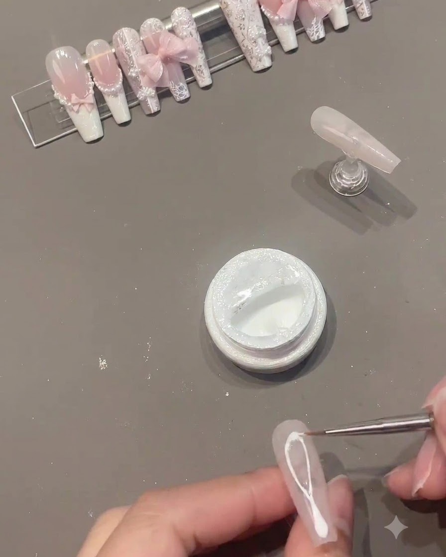 Un pinceau fin traçant des lignes en gel spider blanc au milieu dun ongle en gel rose.