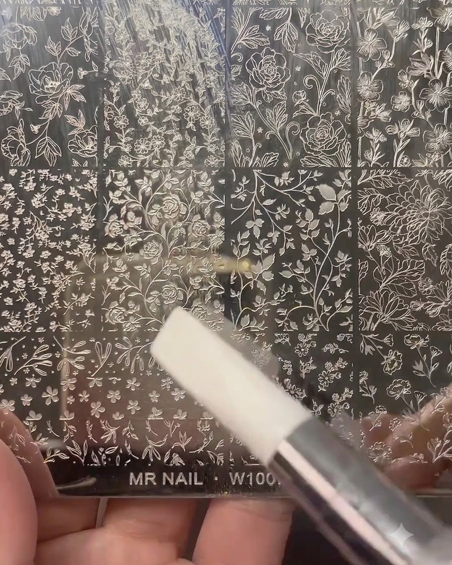 Un tampon dongle transparent pressé sur une plaque de stamping métallique gravée de motifs floraux et botaniques.