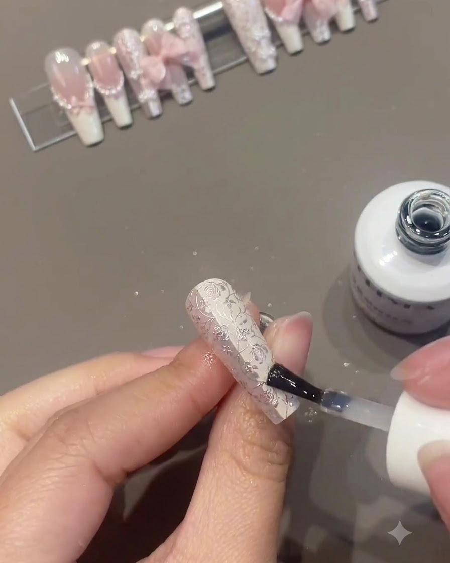 Un pinceau à ongles appliquant un top coat transparent sur un ongle floral richement décoré tandis que dautres ongles finis sont présentés sur un support en arrière-plan.