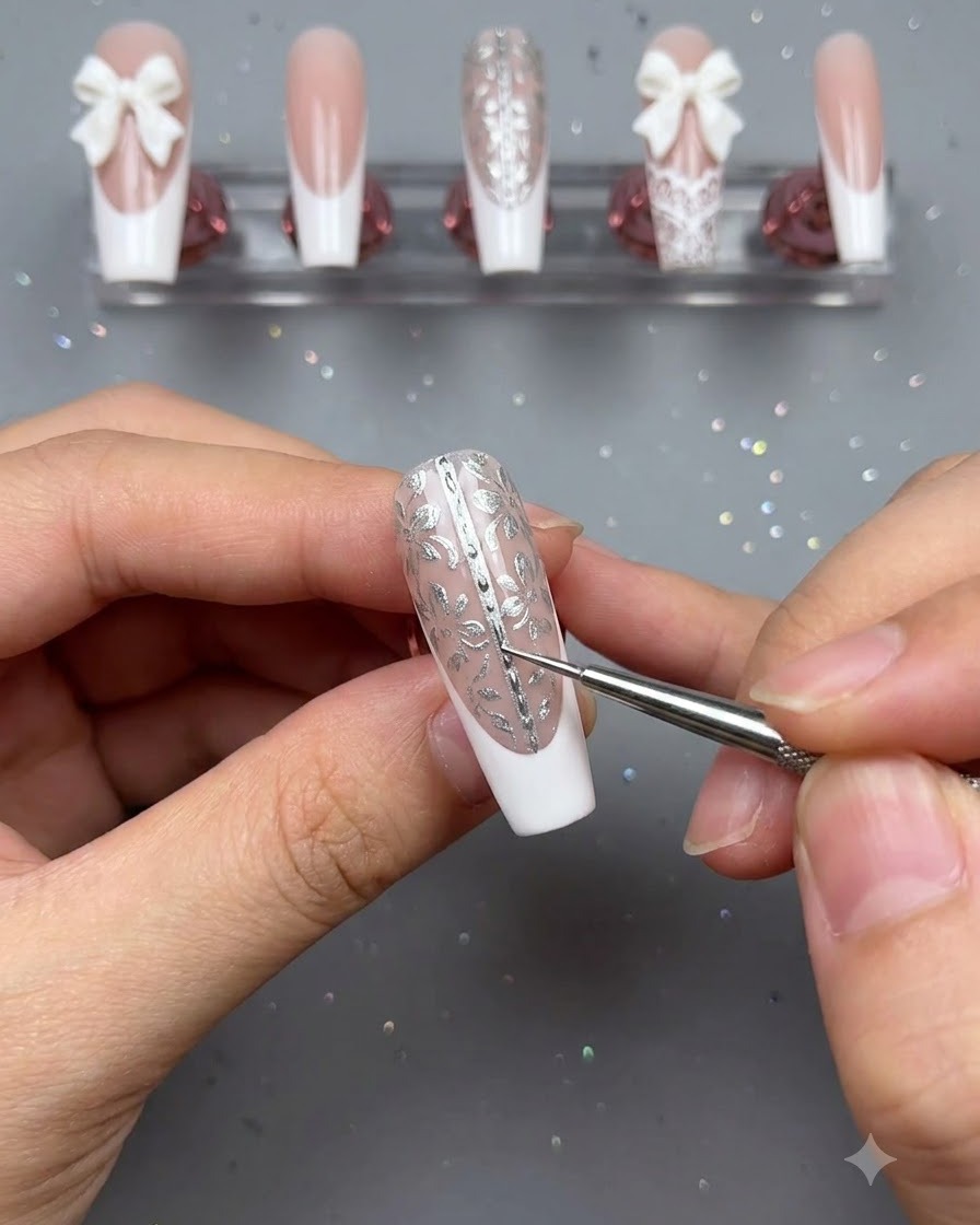 Un pinceau de précision et une pince brucelle utilisés pour placer de minuscules perles le long de la ligne centrale dun faux ongle floral décoré.