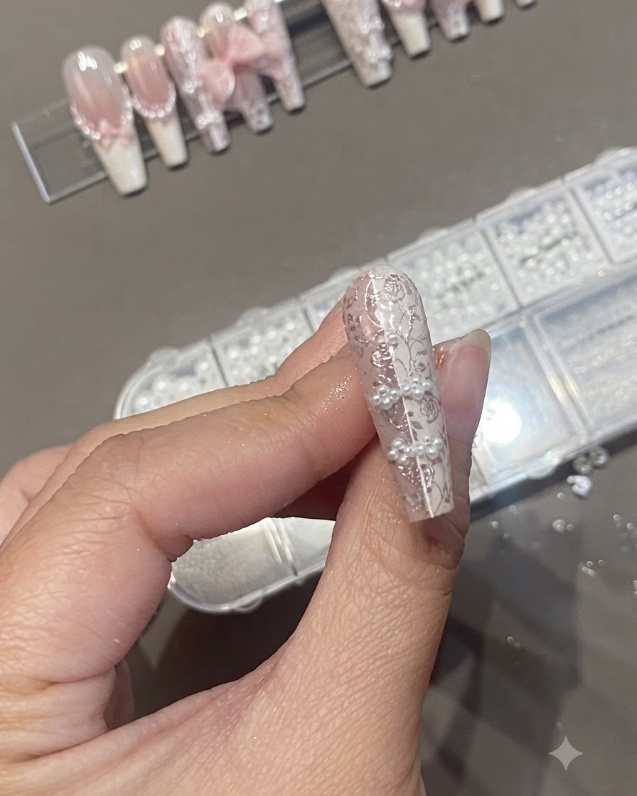Un pinceau à ongles appliquant un top coat transparent sur un design dongle texturé agrémenté de perles et de stamping en dentelle.