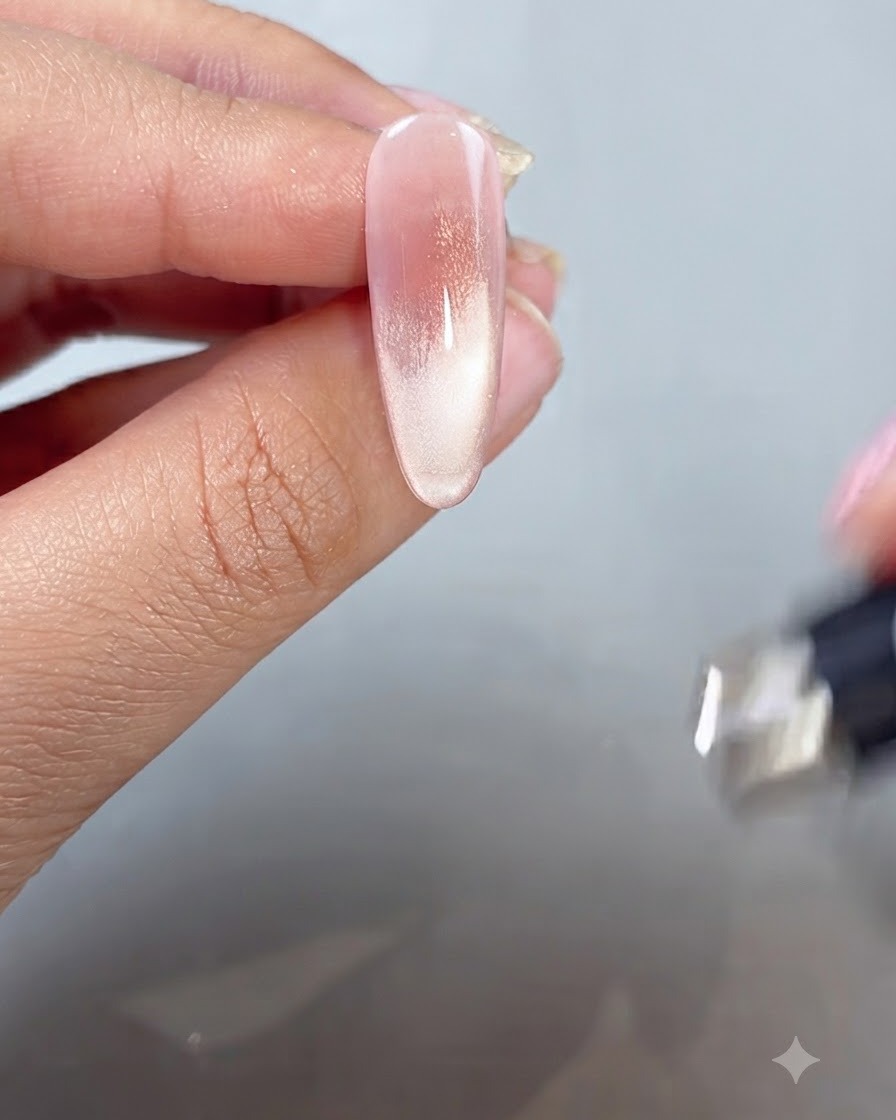 Une baguette magnétique tenue près dun doigt peint pour façonner le reflet cat-eye dans un style French tip.