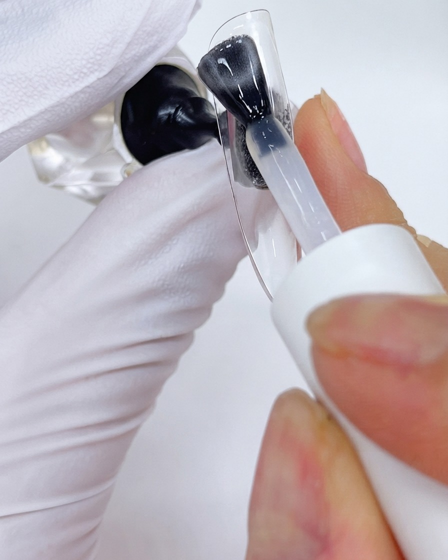 Un pinceau appliquant une couche de top coat sur un présentoir à ongles transparent.