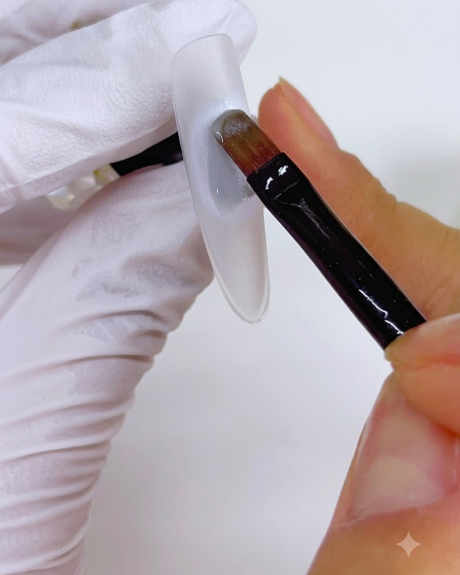 Un pinceau appliquant une couche de gel sur une base de perle circulaire sur un ongle.