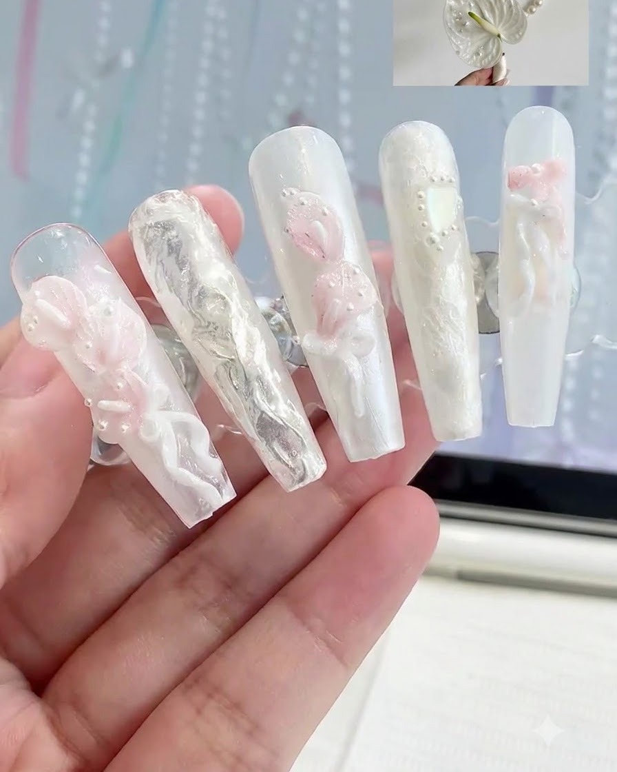 Un support de présentation contenant plusieurs faux ongles avec divers designs de nail art floral 3D blanc et rose.