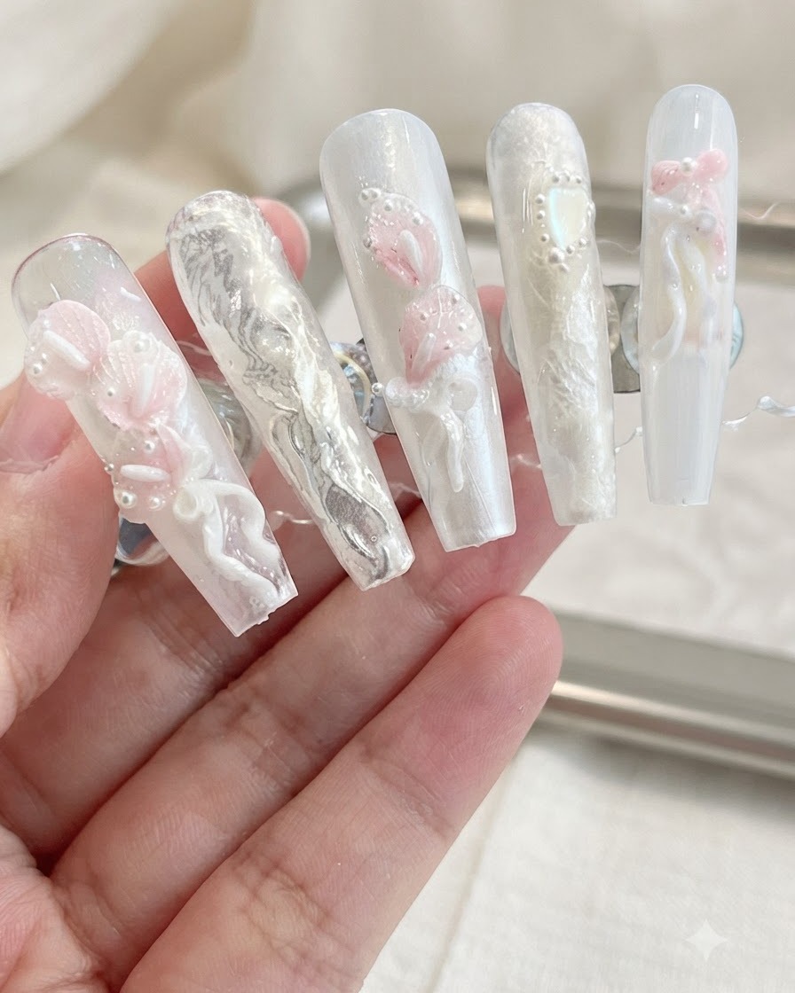 Une présentation de faux ongles finis arborant des lys callas 3D, des nœuds et des embellissements de perles sur un fond neutre.
