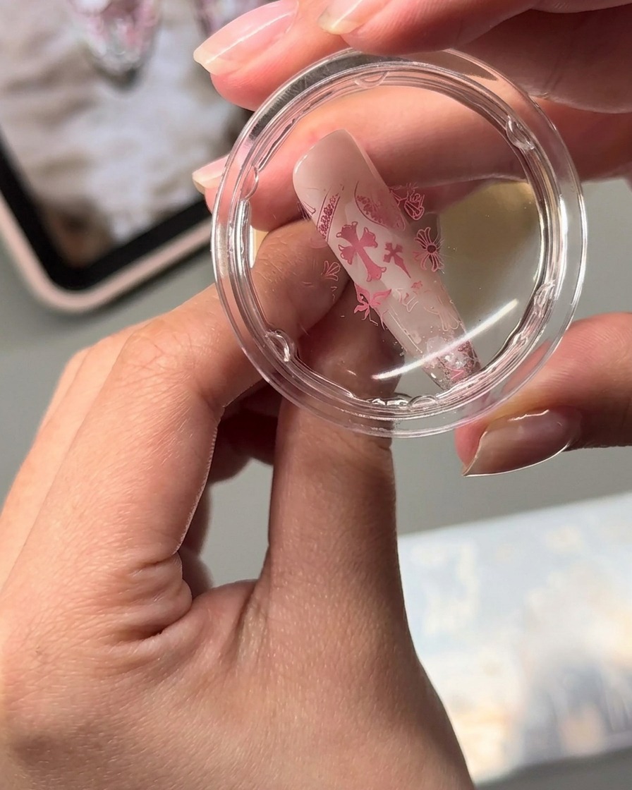 Un tampon jelly transparent transférant des motifs dart dongle roses estampés sur un ongle en amande.