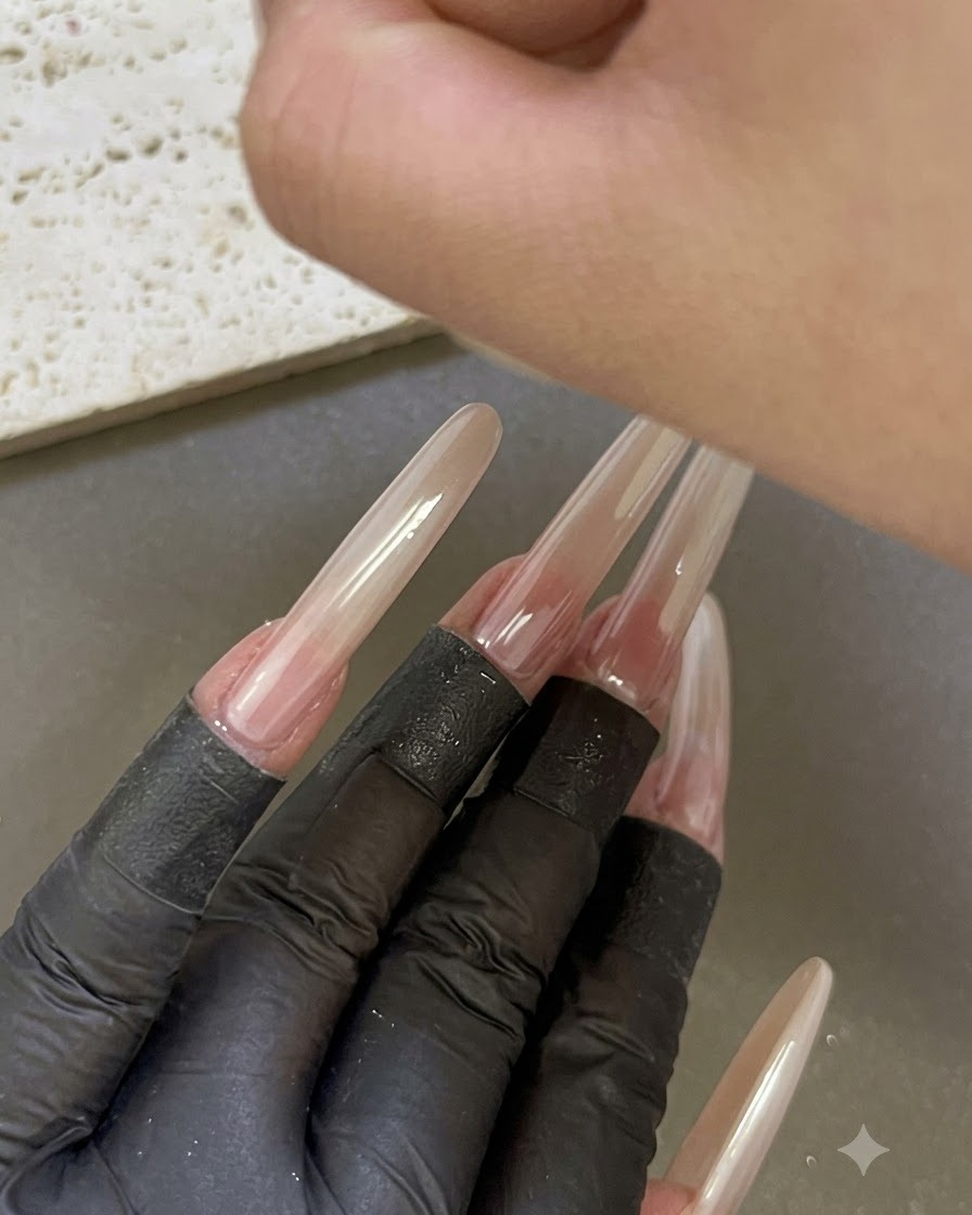 Une main placée sous une lampe à ongles UV/LED avec dautres doigts manucurés rallongés visibles au premier plan.