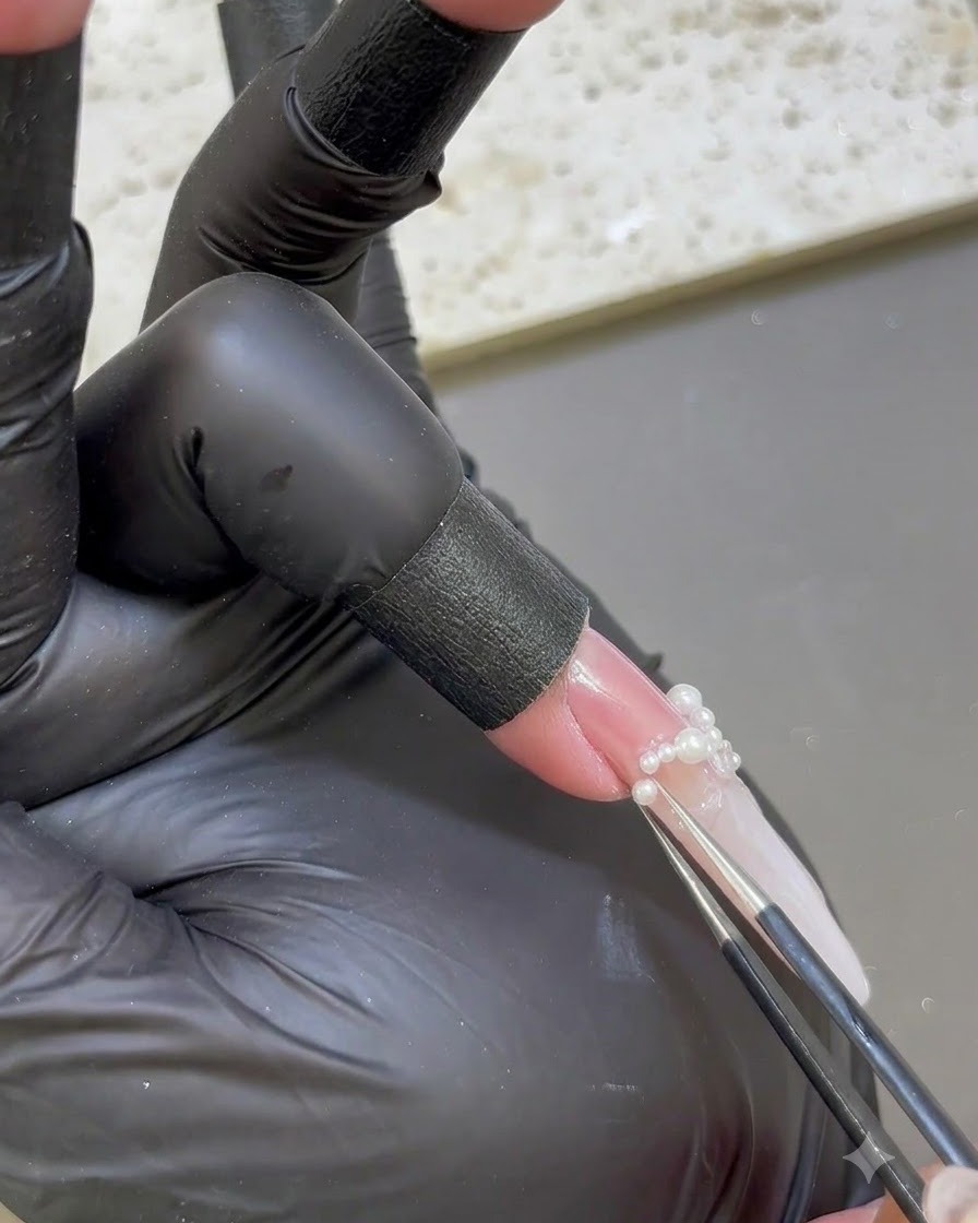 Une pince de précision plaçant de petites perles blanches à la base dun ongle rallongé.