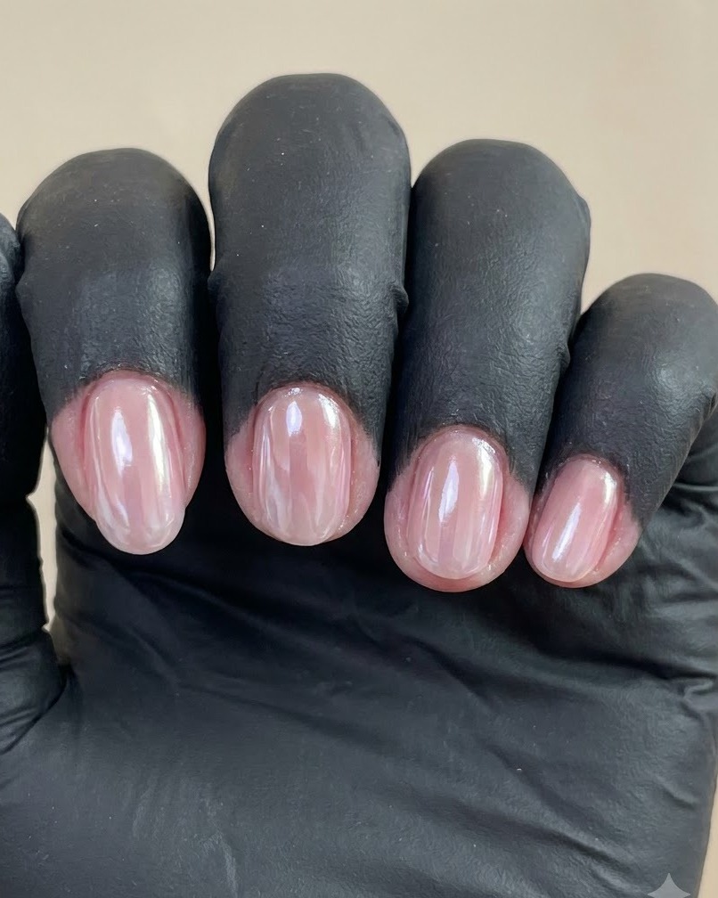 Une vue rapprochée dune main gantée montrant quatre ongles manucurés avec un fini chrome perle brillant sur un fond uni.