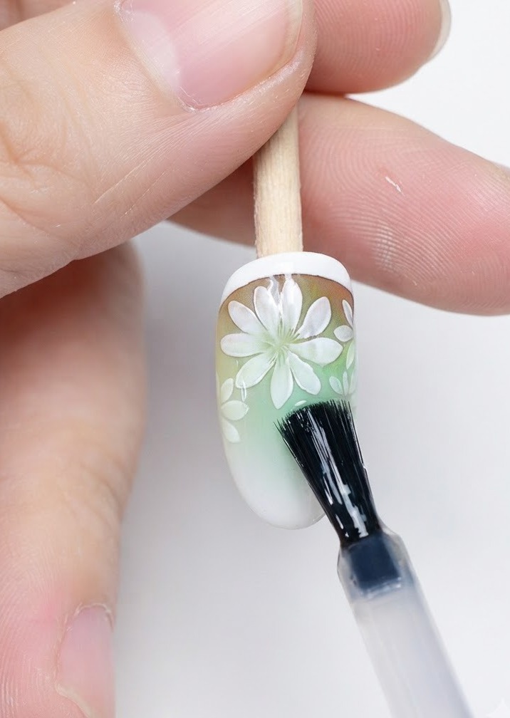 Un pinceau appliquant un top coat mat par-dessus le nail art marguerite terminé.