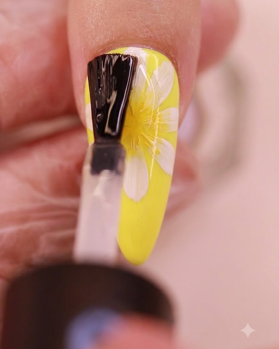 Un pinceau appliquant une couche transparente de top coat sans résidu sur le design dongle marguerite peint.