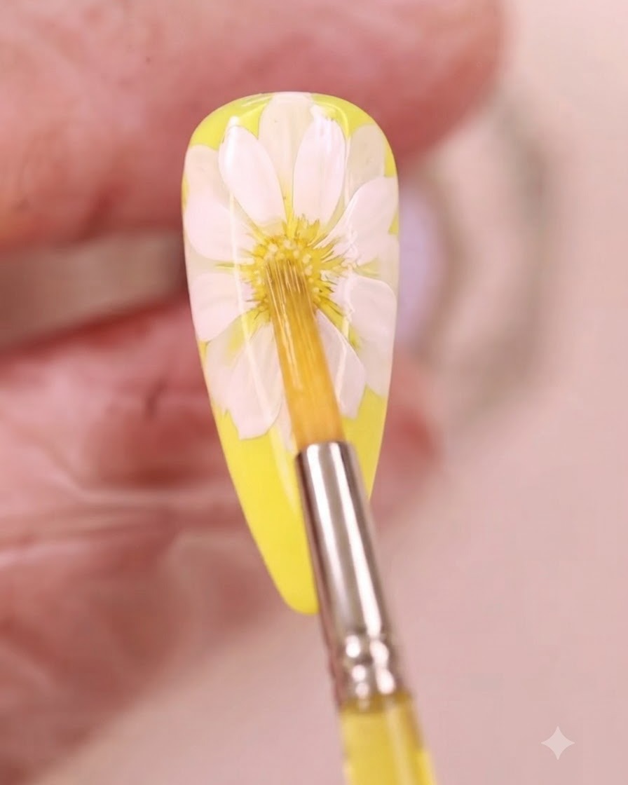 Un pinceau fin appliquant du liquide aquarelle jaune au centre dun design dongle marguerite blanche.