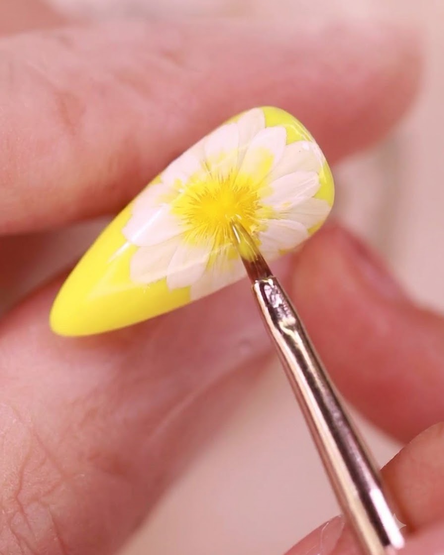 Un pinceau de détail fin appliquant un top coat transparent sur un design dongle floral.