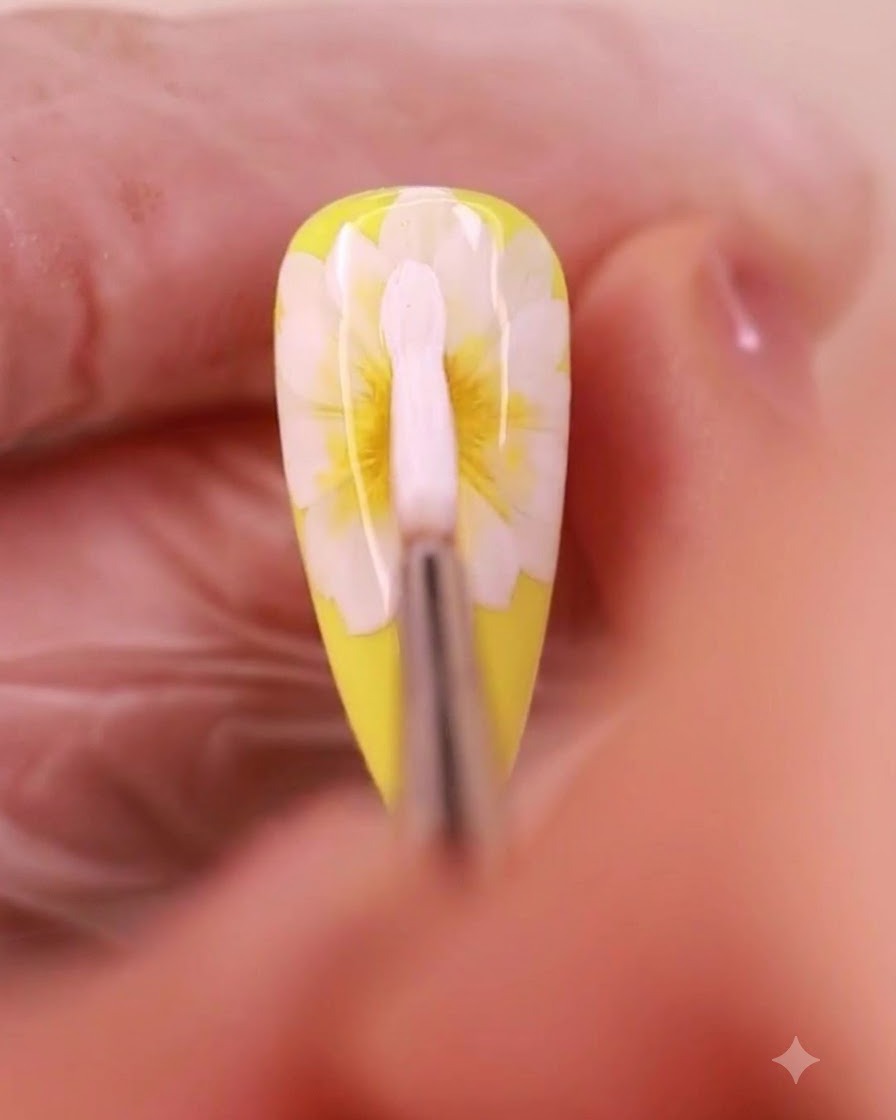 Un pinceau de nail art appliquant du gel blanc pour former une troisième couche de pétales sur un design de marguerite.