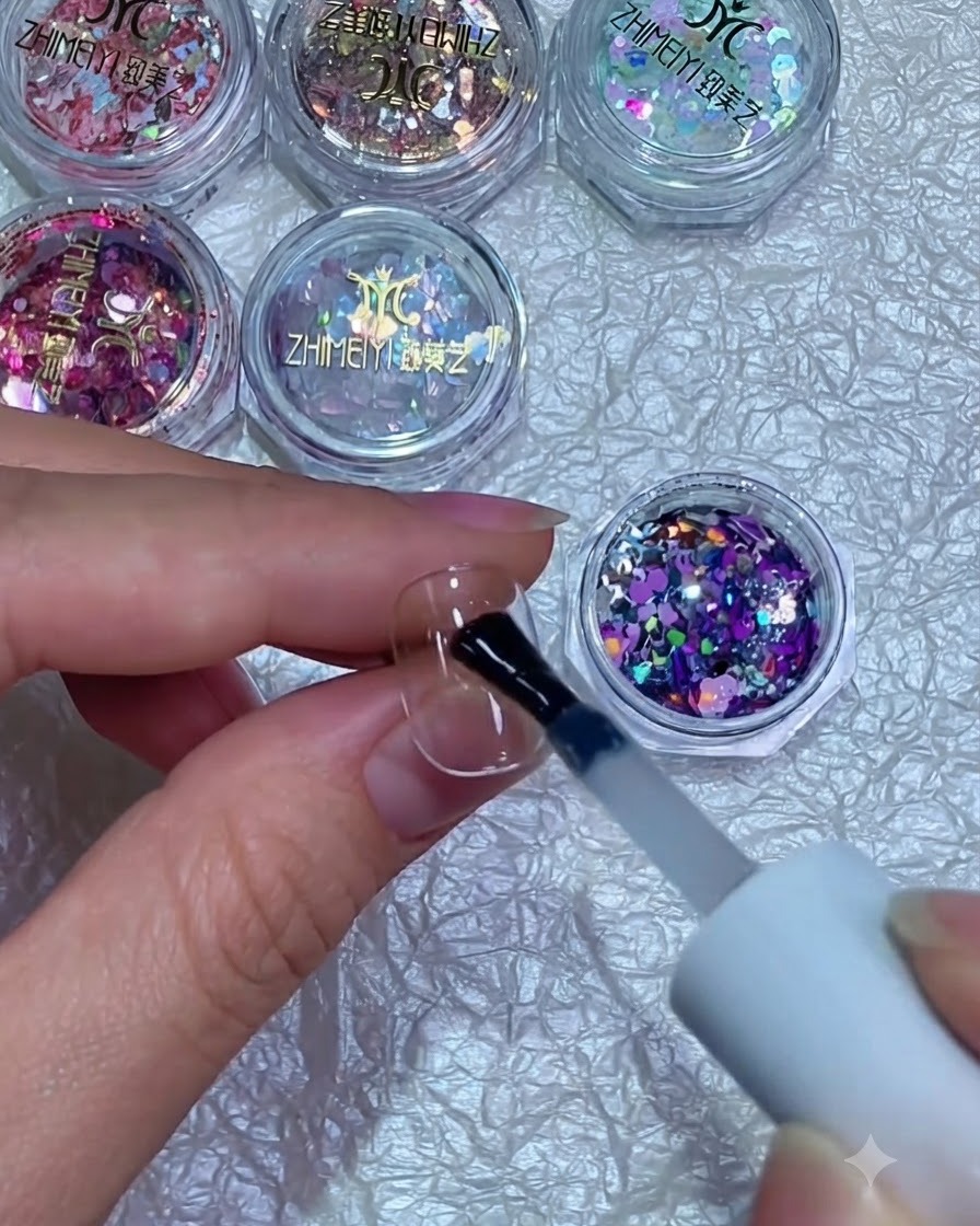 Un pinceau tenant des paillettes mélangées violettes et argentées au-dessus dun ongle recouvert de gel humide.
