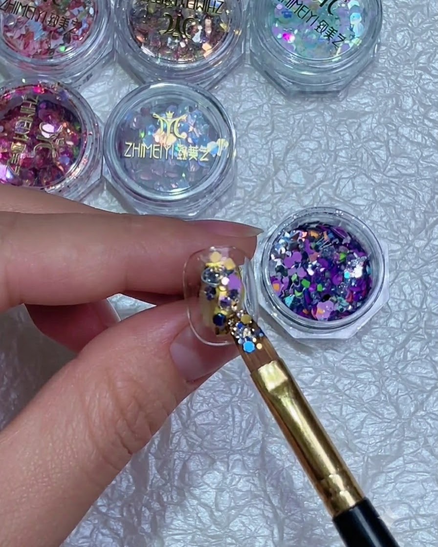 Un pinceau ajustant précisément la position des paillettes colorées sur un ongle.