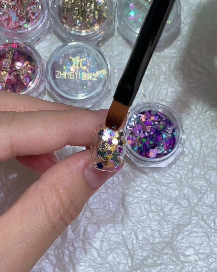 Un gros plan dune main avec un nail art pailleté placée sous une lampe de catalysation.