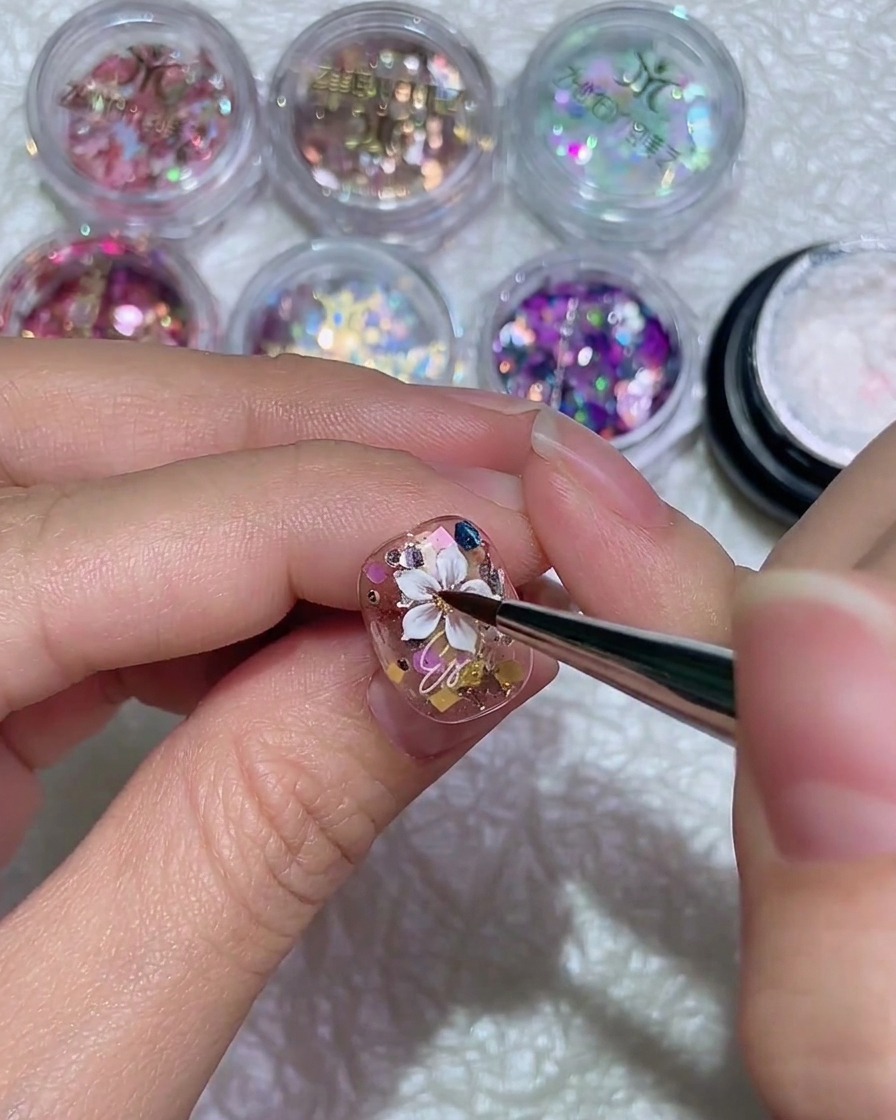 Un pinceau fin trace un seul pétale blanc pour un design de marguerite sur un ongle brillant.