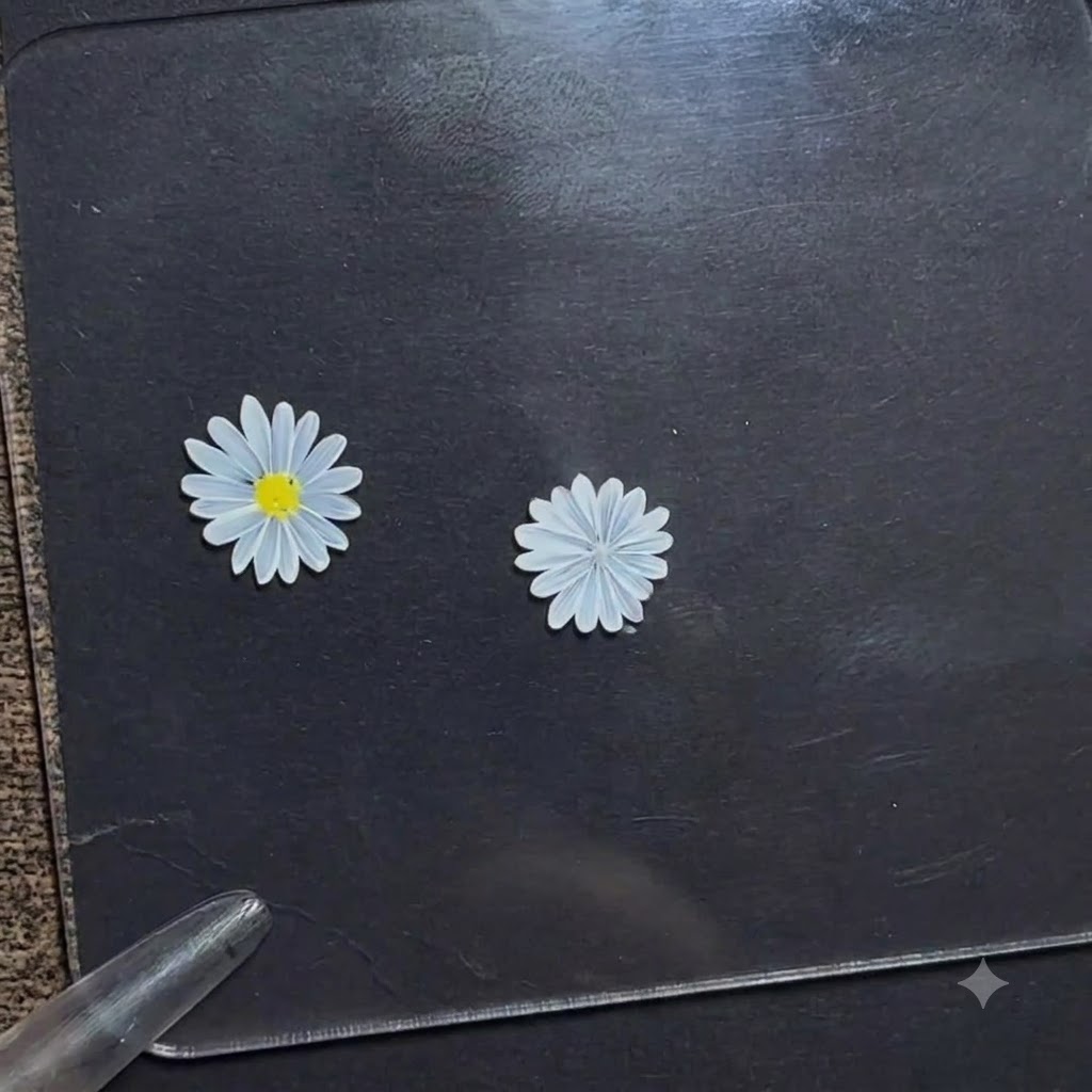 Un stylo de dotting appliquant un petit point de gel jaune vif au centre dune fleur de marguerite blanche sur un panneau de présentation sombre.