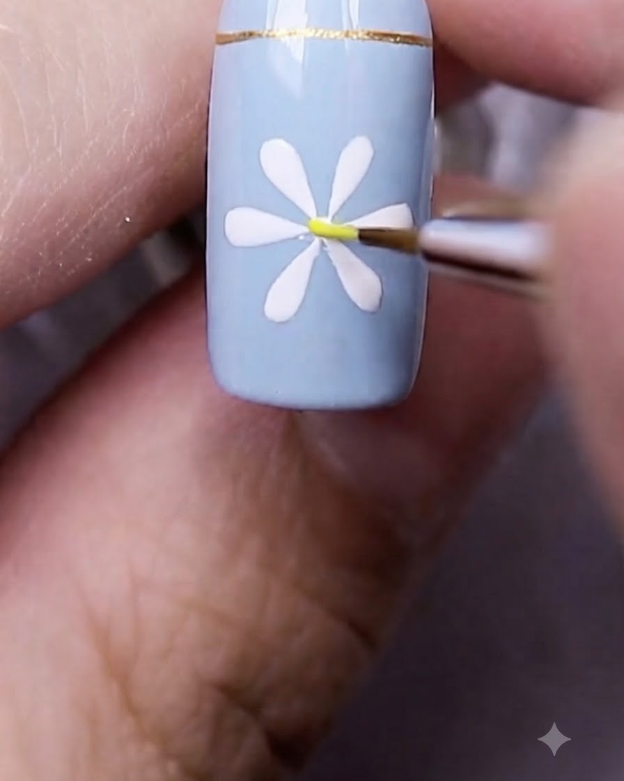 Un pinceau nail art fin plaçant un petit point jaune directement au centre de la marguerite blanche peinte.