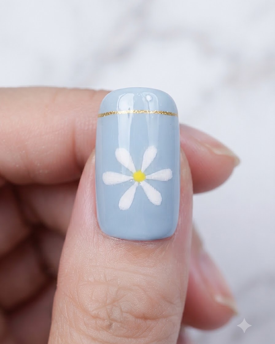 Un pinceau appliquant un top coat transparent et brillant sur un ongle bleu terminé avec un design de marguerite.