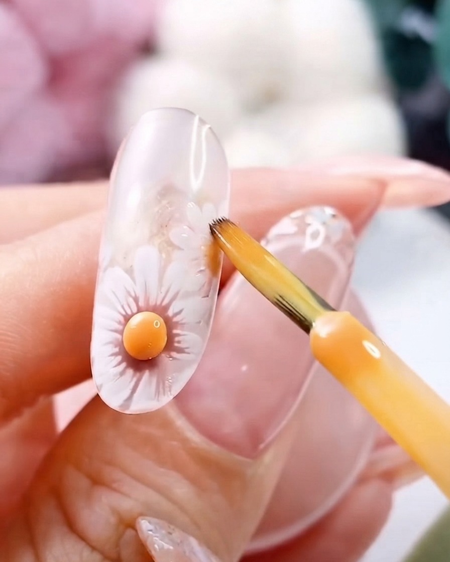Un pinceau fin près dun centre de fleur jaune 3D catalysé sur un ongle en gel transparent.
